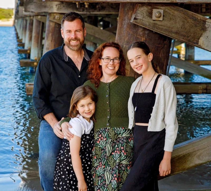 Family of four standing together under a wooden pier by water