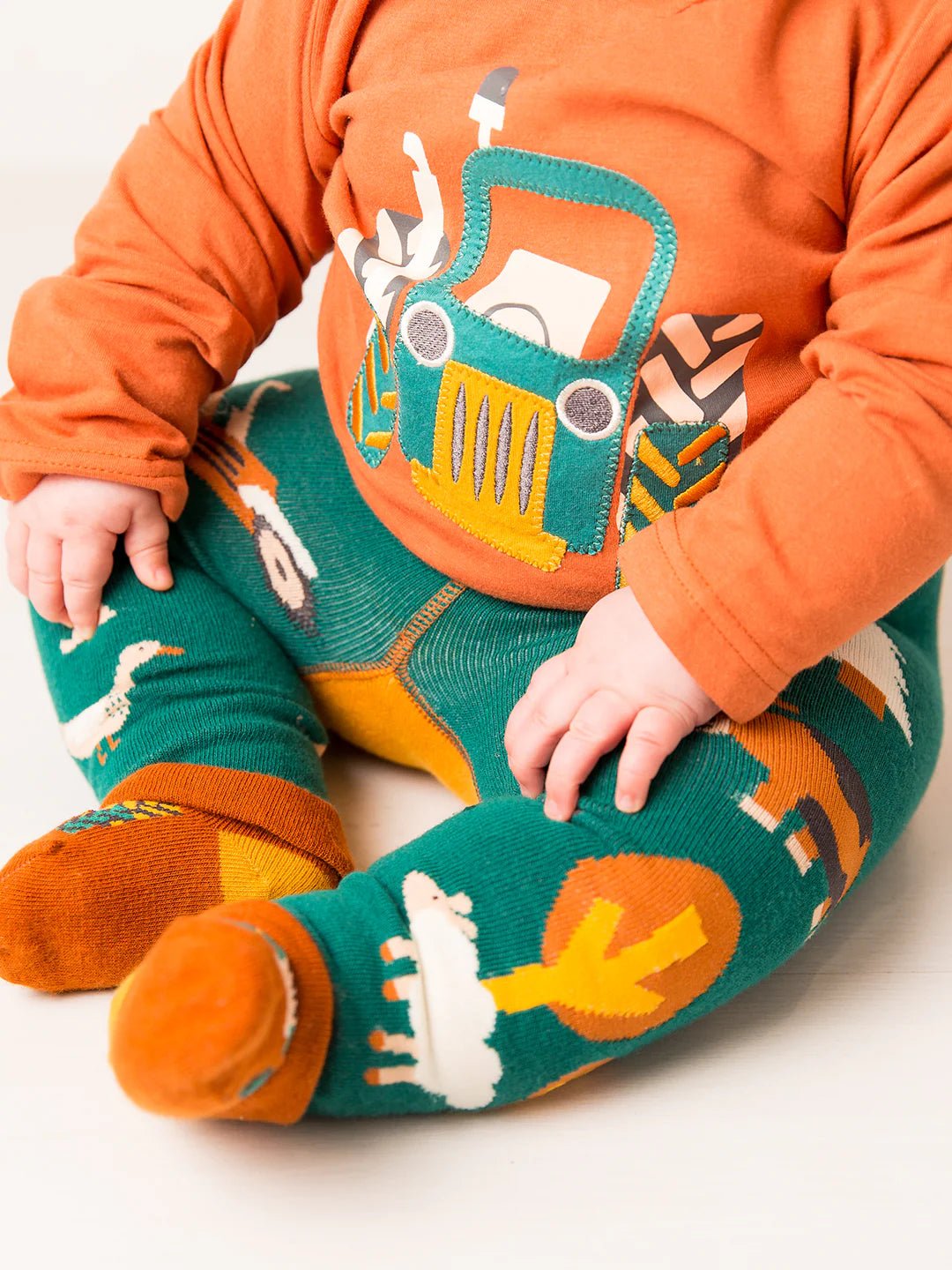 Child wearing an orange shirt with a truck design and green pants with animal prints on a white background