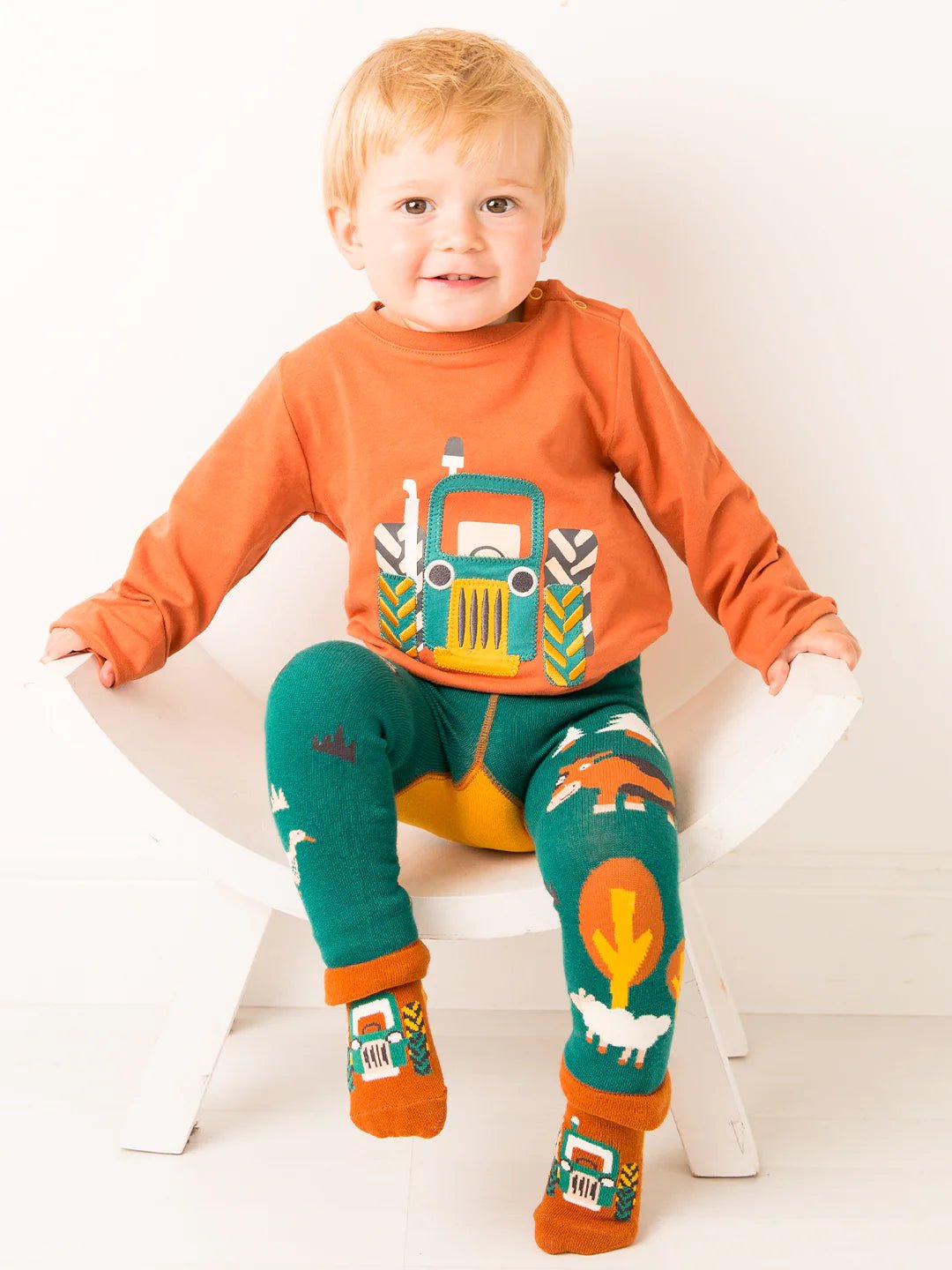 Child wearing an orange shirt with a truck design, green leggings with animal prints, and orange socks with vehicle designs.