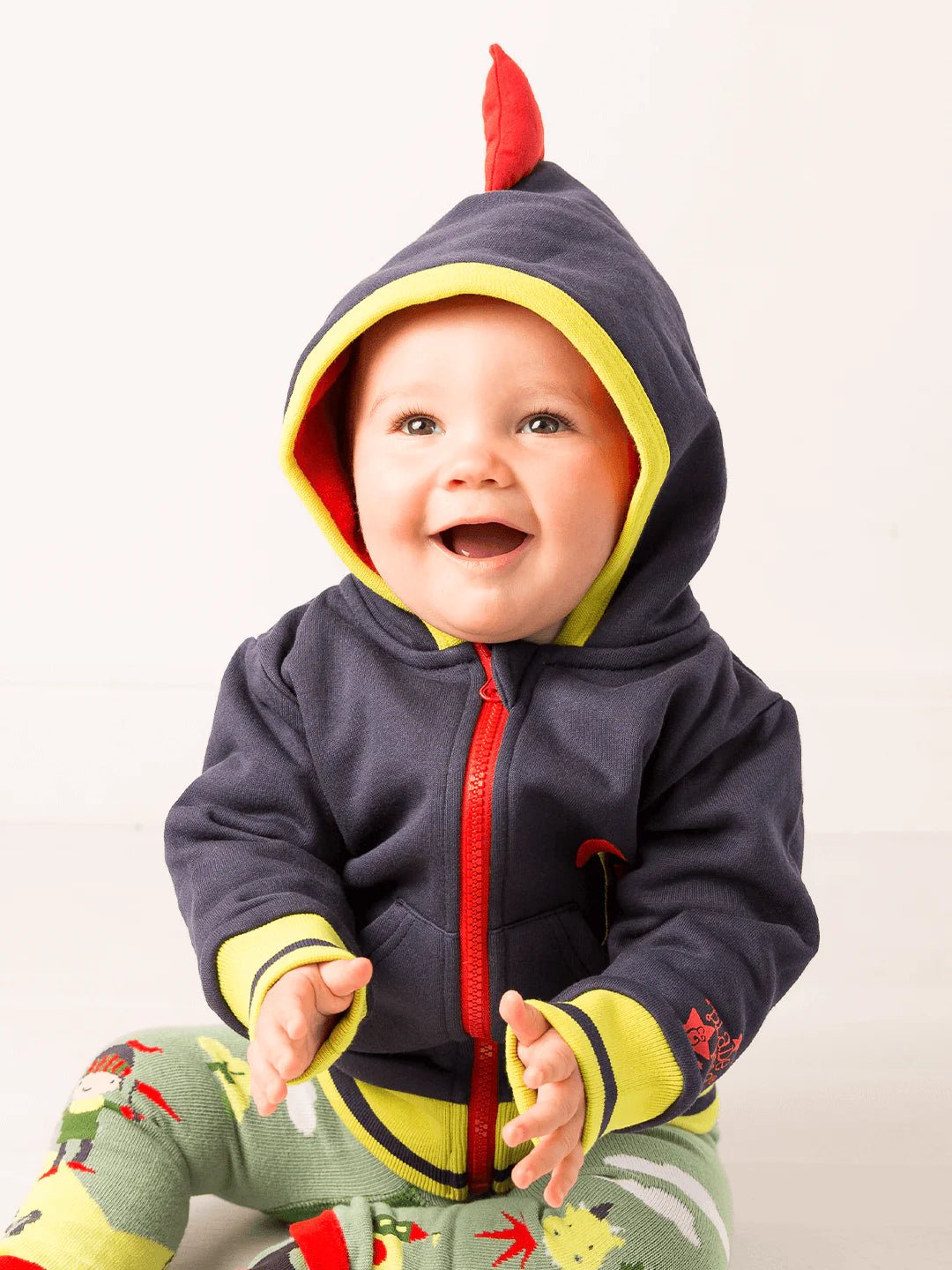 Baby wearing a colorful hoodie with a red hood and yellow accents on a white background