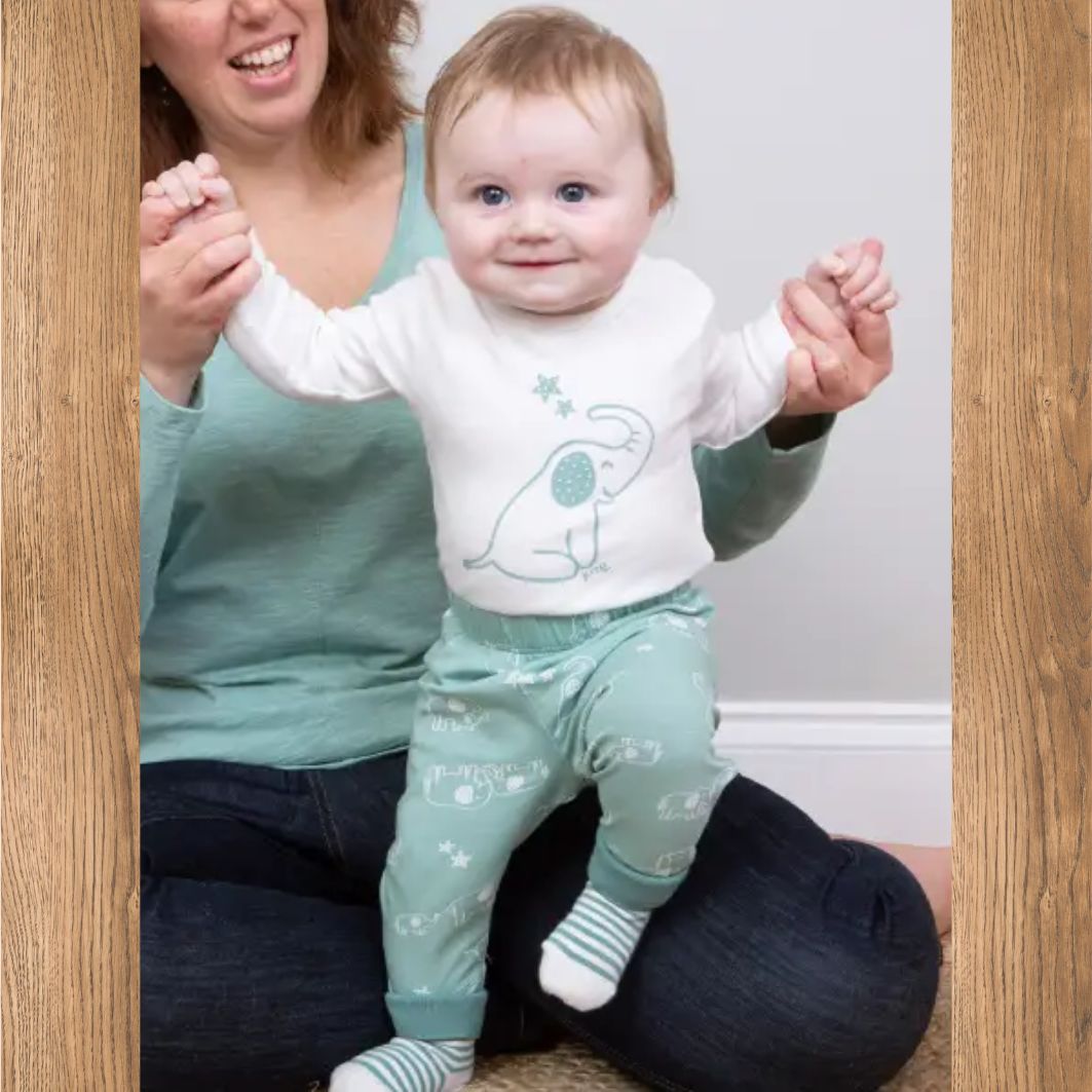 Baby in matching outfit with adult holding hands, standing in doorway.