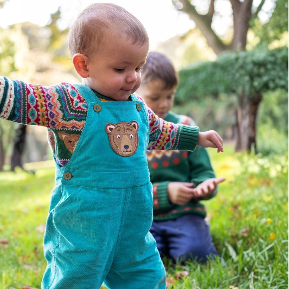 Child wearing teal overalls with a bear patch outdoors