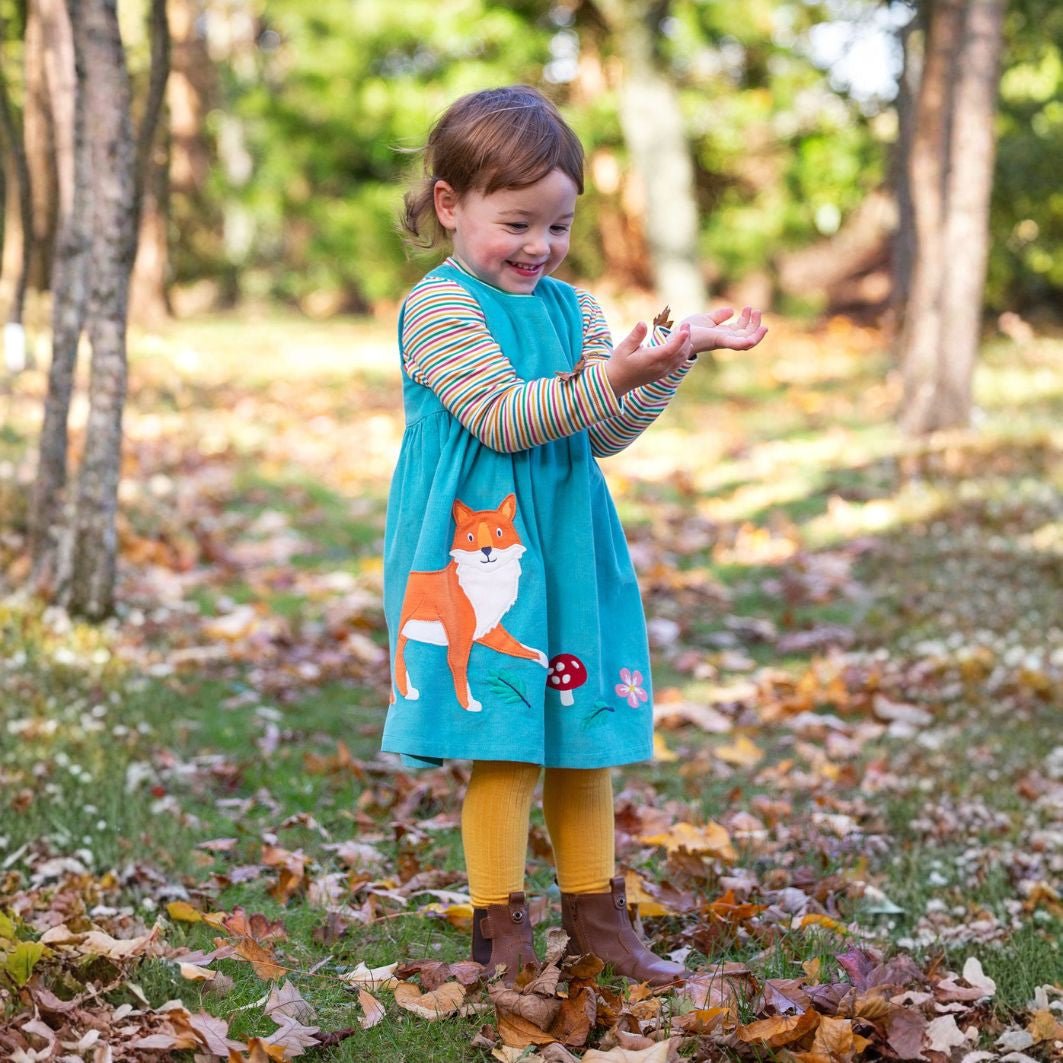 Child wearing a turquoise dress with a fox design in an autumn setting