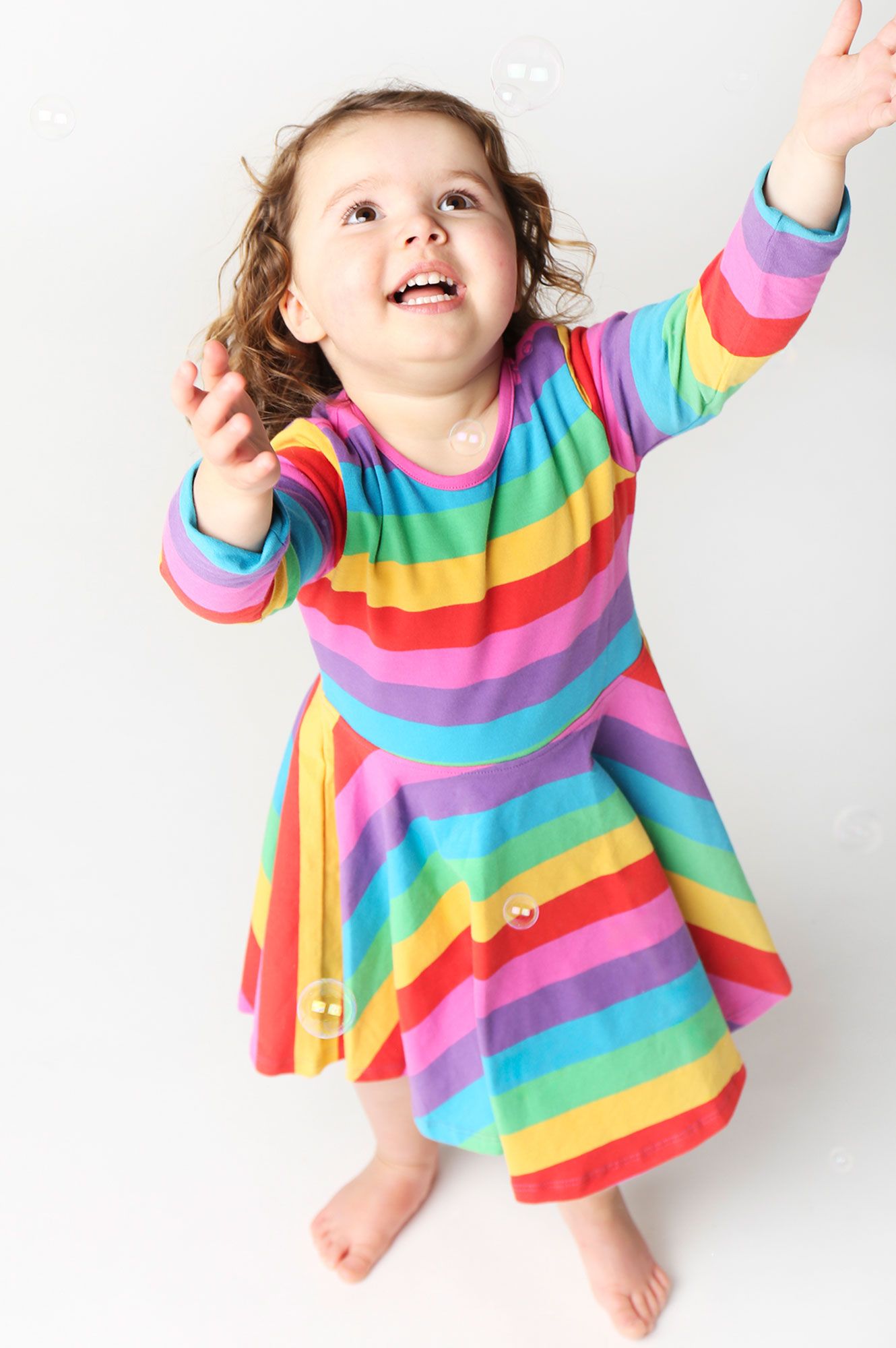 Child wearing a colorful rainbow dress against a white background