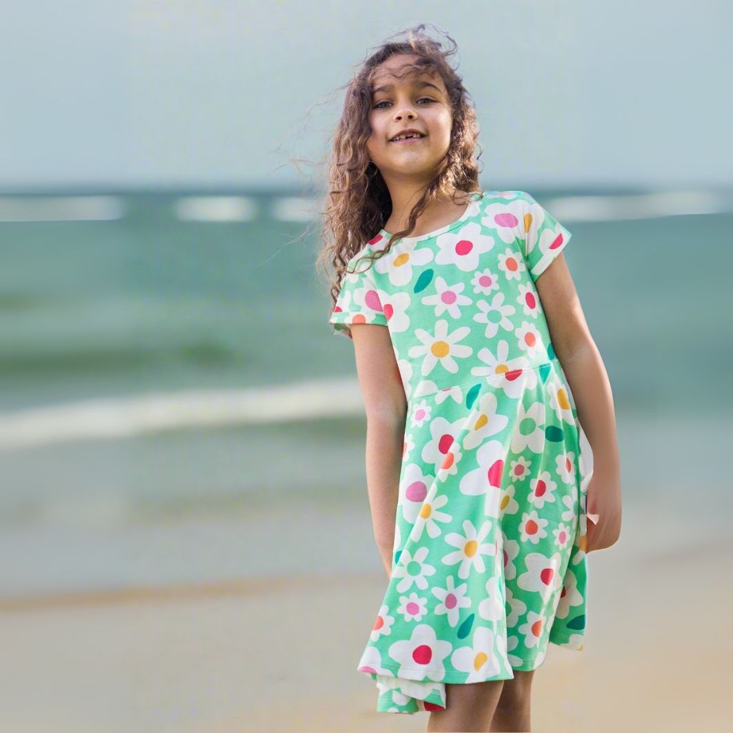 Young girl wearing a floral dress standing on a beach.