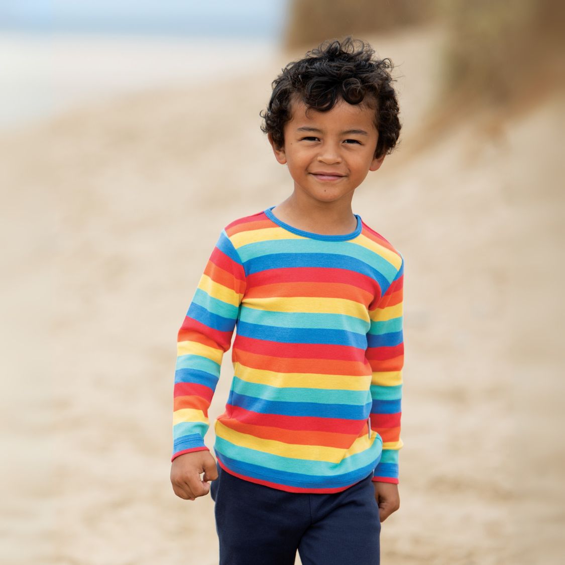 Child wearing a rainbow striped shirt on a beach
