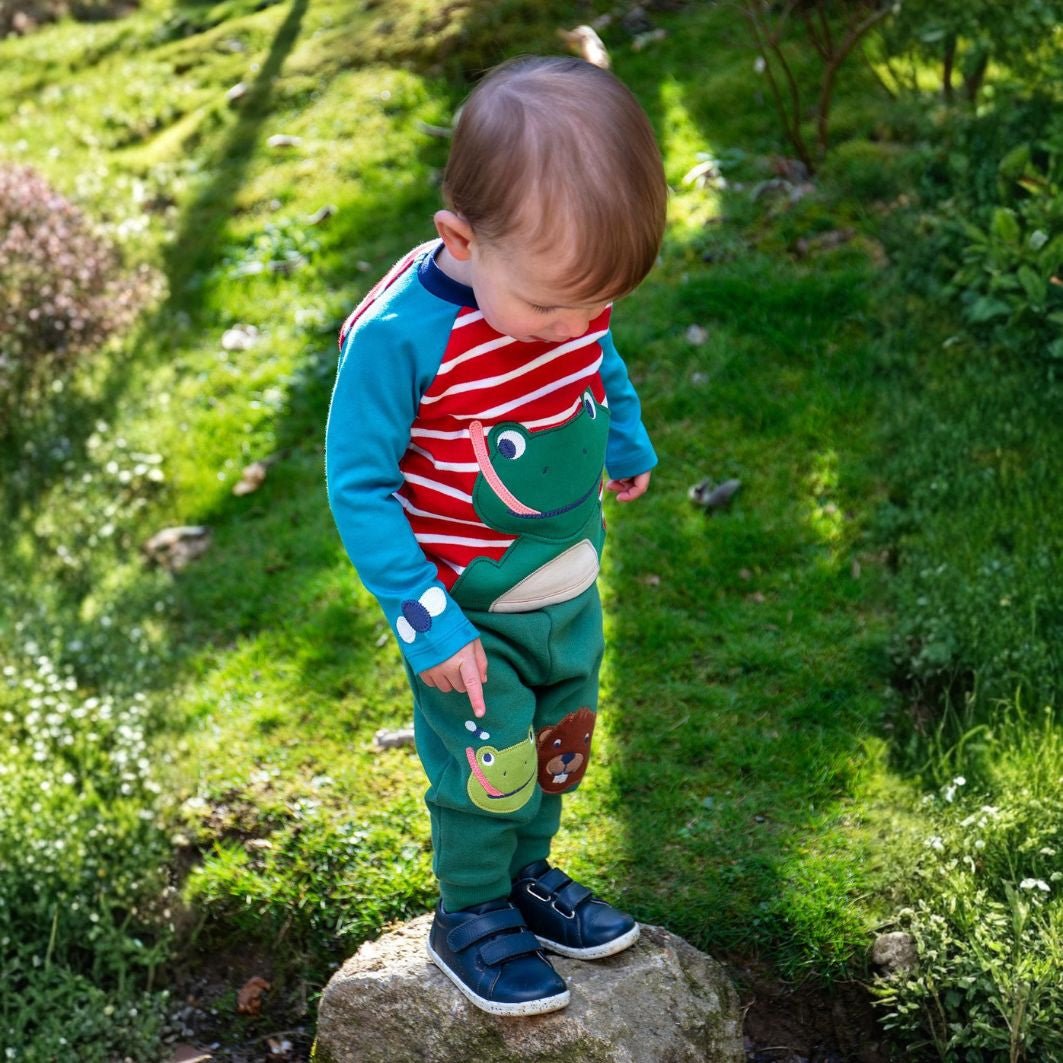 Child wearing a colorful outfit with animal designs standing on a rock in a garden.