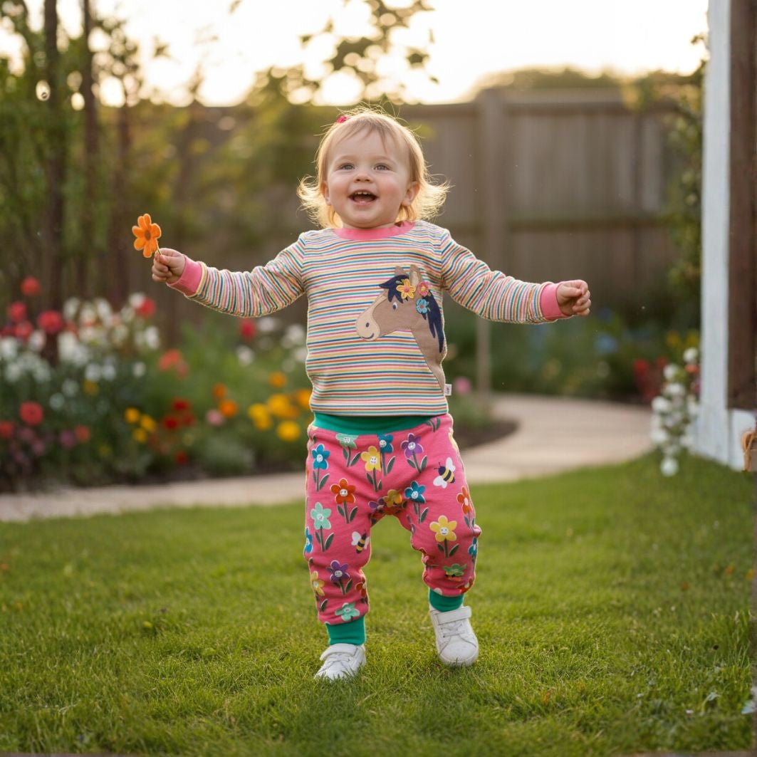 Child in a garden wearing a colorful outfit with a unicorn design.