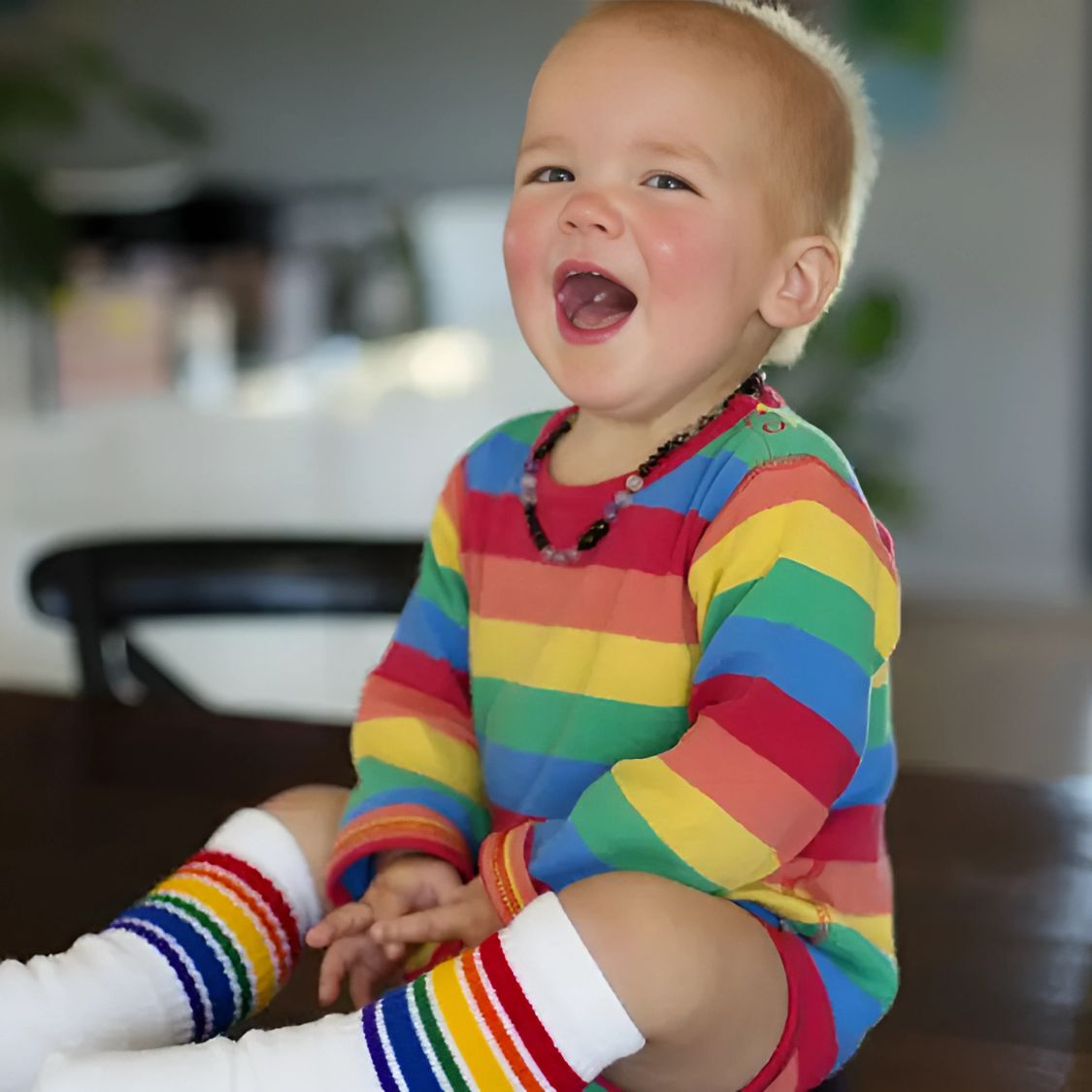 Child wearing a rainbow striped outfit sitting on a couch.