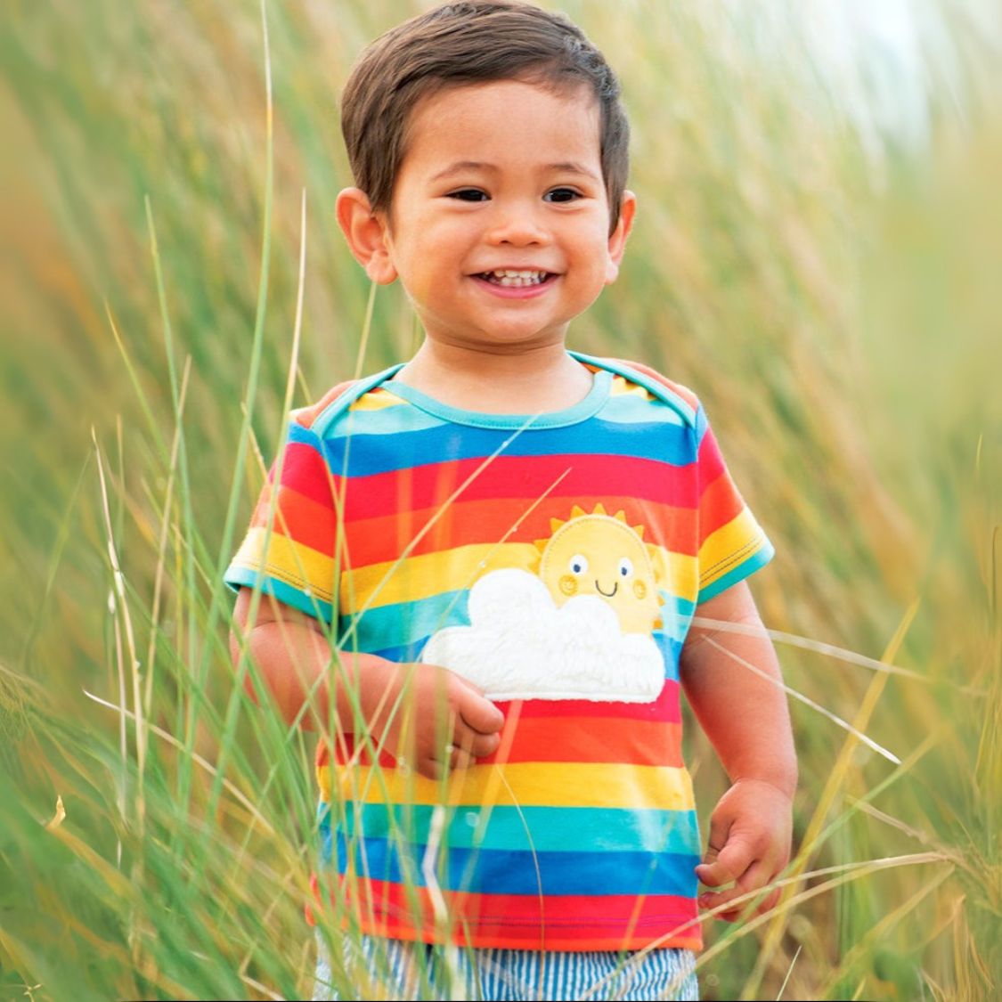 Child wearing a colorful striped shirt with a cloud design in a grassy field