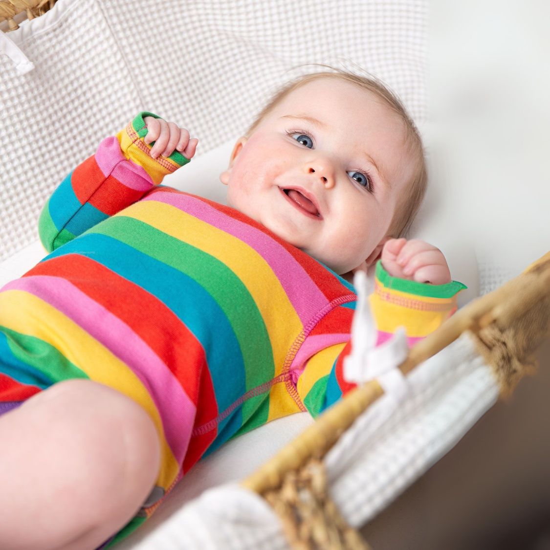Baby wearing a colorful striped outfit lying on a white blanket.