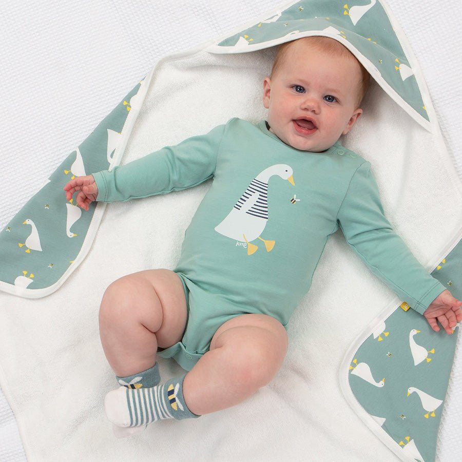 Baby in a green onesie with duck design lying on a white blanket