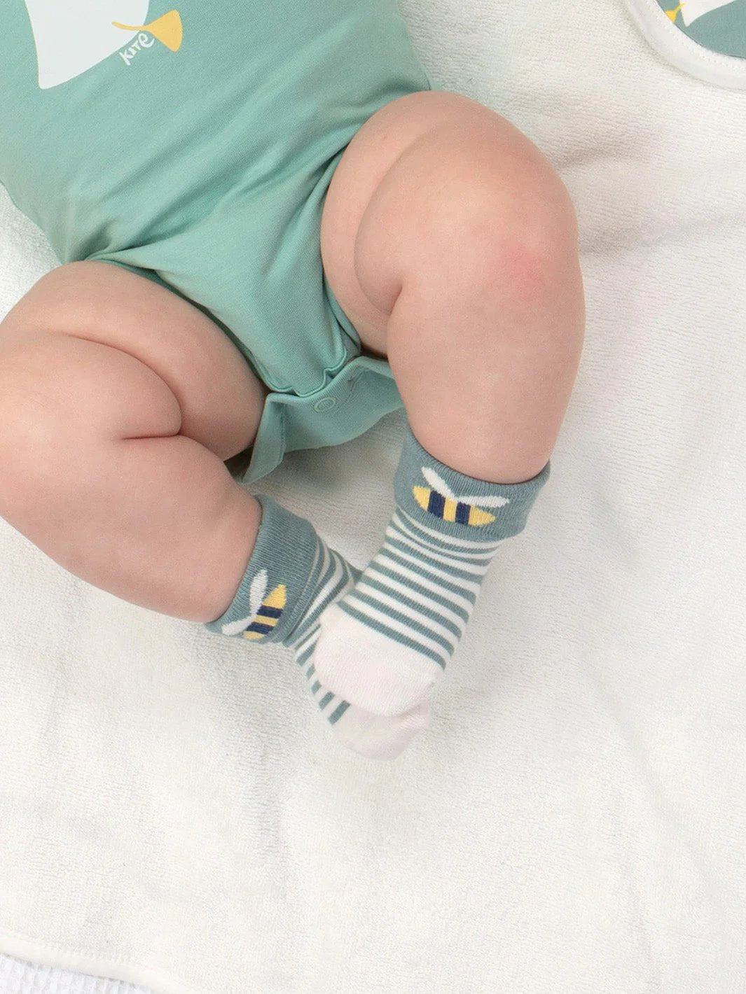 Baby wearing green shorts and striped socks with bee design on a white blanket