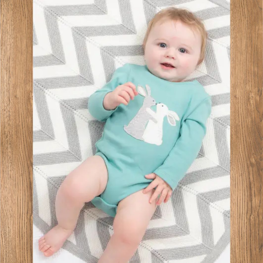 Baby wearing a light blue onesie with a white bunny design on a chevron-patterned rug.
