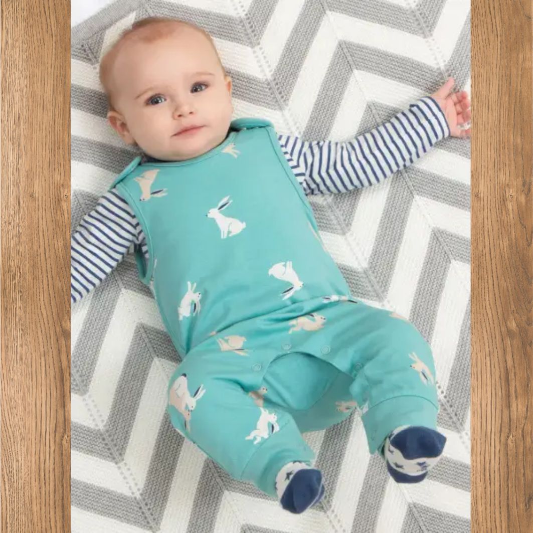 Baby lying on a chevron-patterned rug wearing a teal outfit with rabbit prints