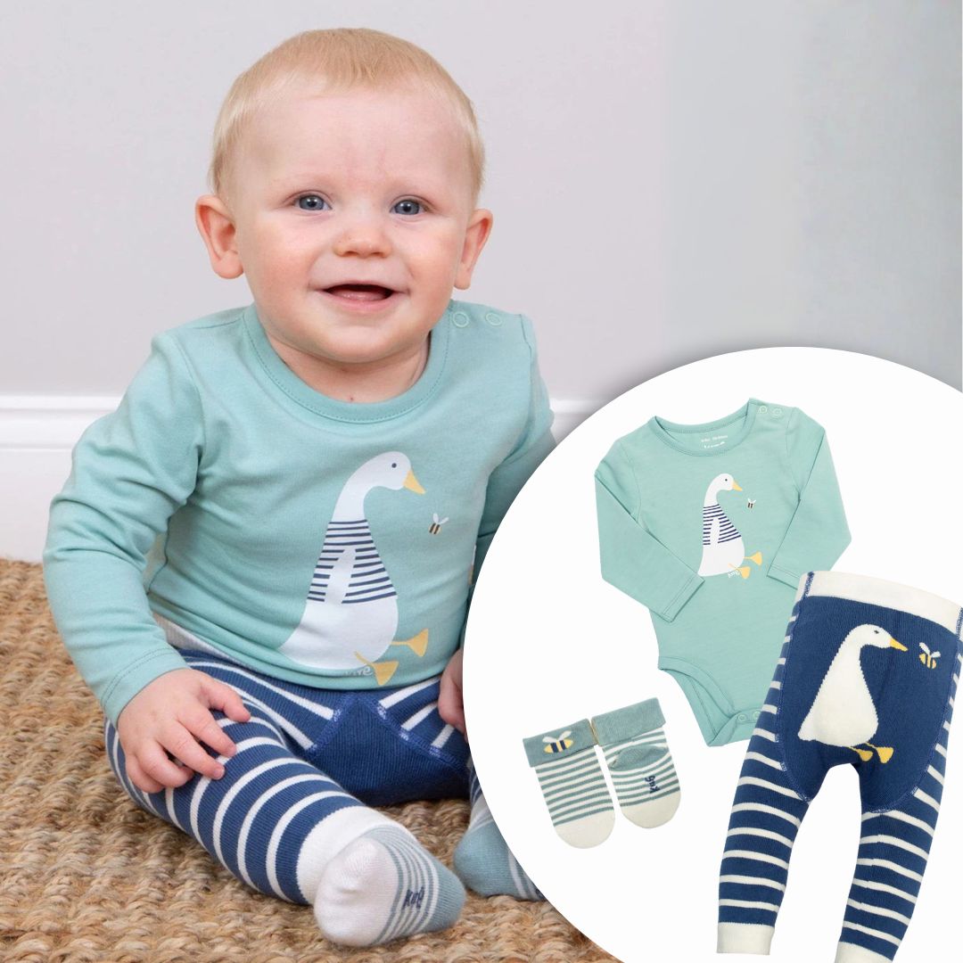 Baby wearing a light blue onesie with a duck design, sitting on a carpeted floor.