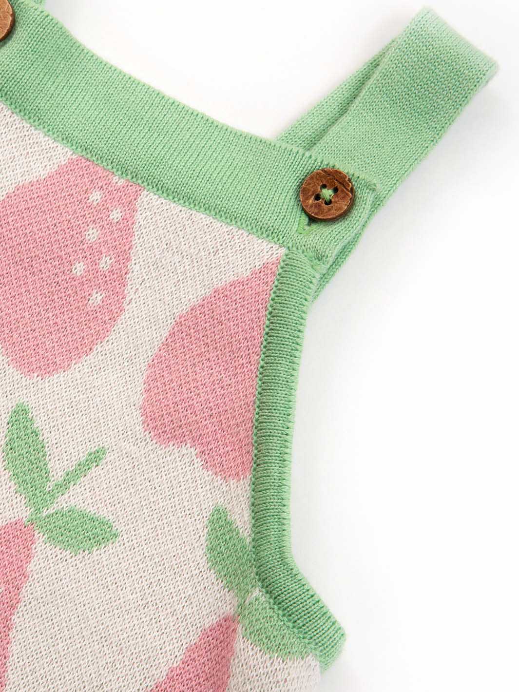 Close-up of a baby romper with strawberry pattern and green straps on a white background