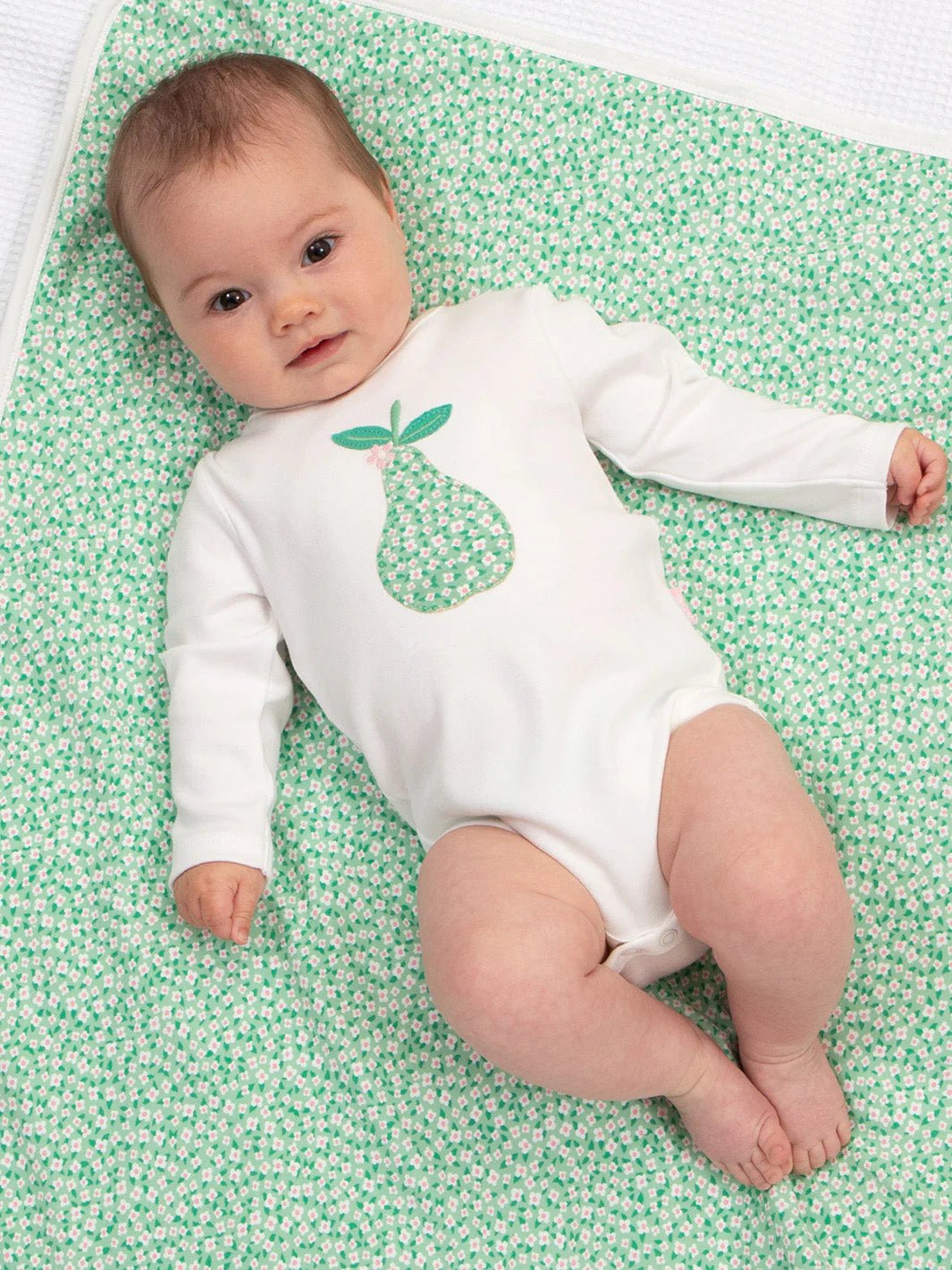Baby wearing a white onesie with a green pear design on a green patterned blanket