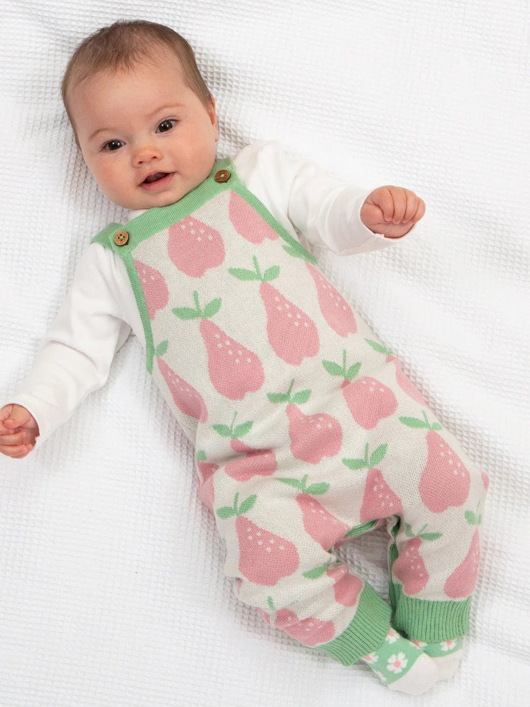 Baby wearing a romper with pink pear pattern on a white background