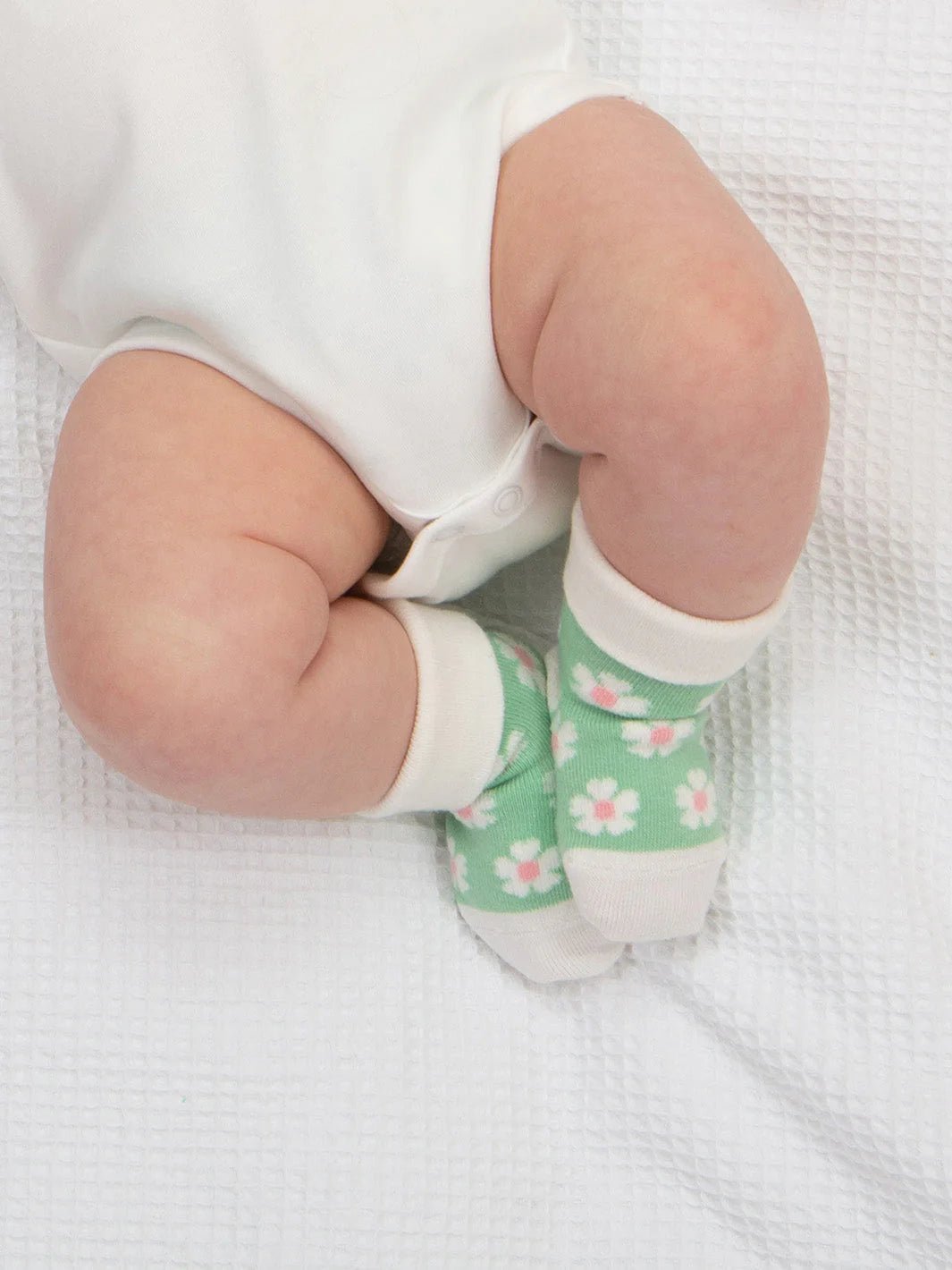 Baby's legs wearing green socks with floral patterns on a white background