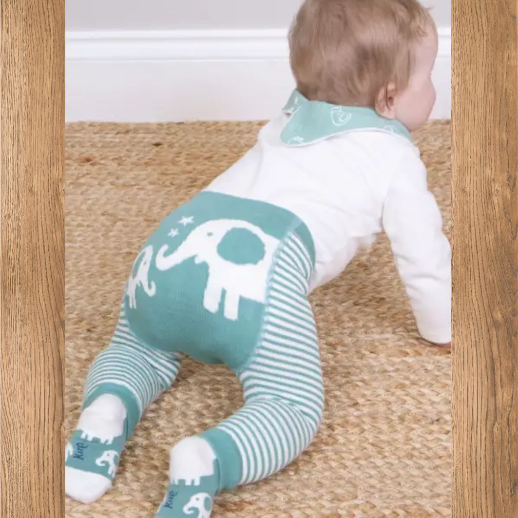 Baby in a white and teal outfit with elephant design on a wooden floor.