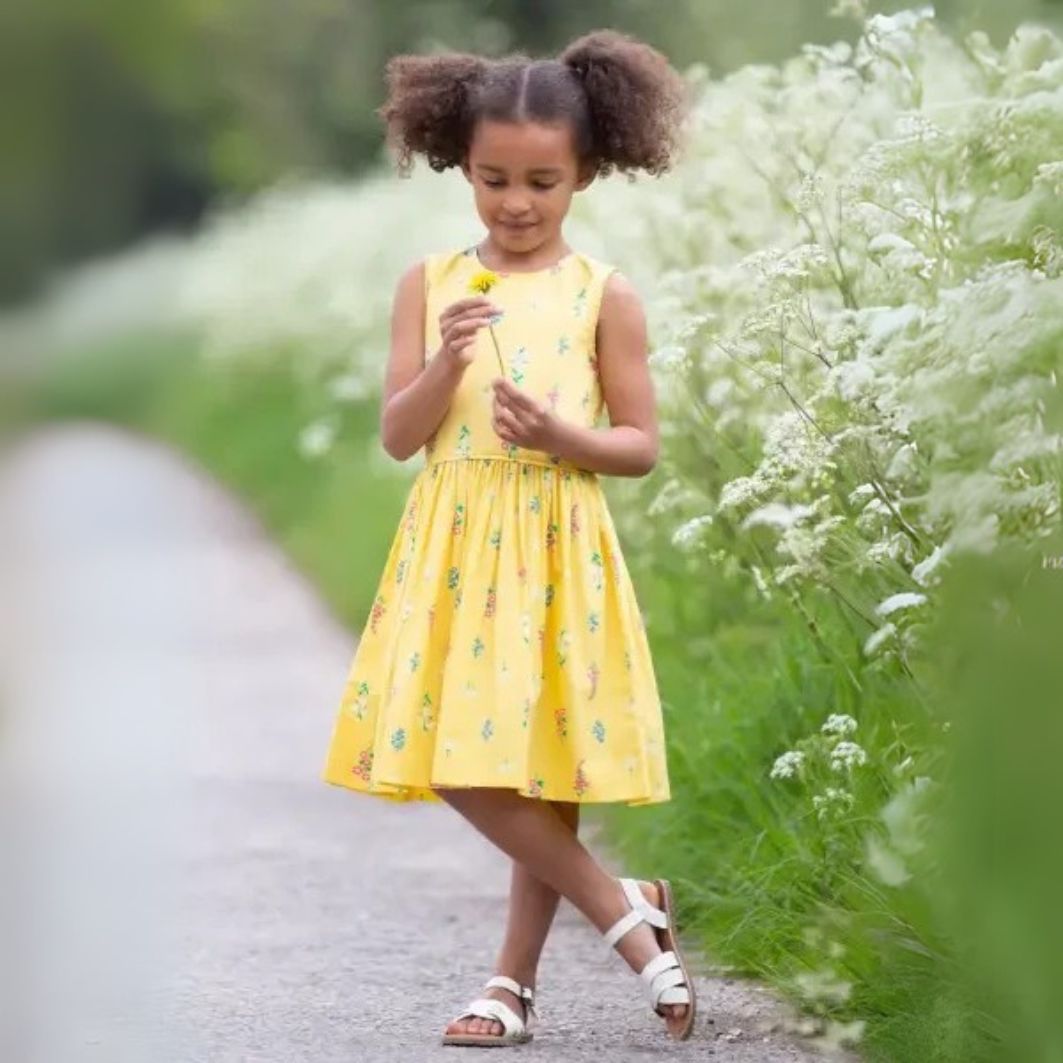 Young girl in a yellow dress standing on a path surrounded by greenery