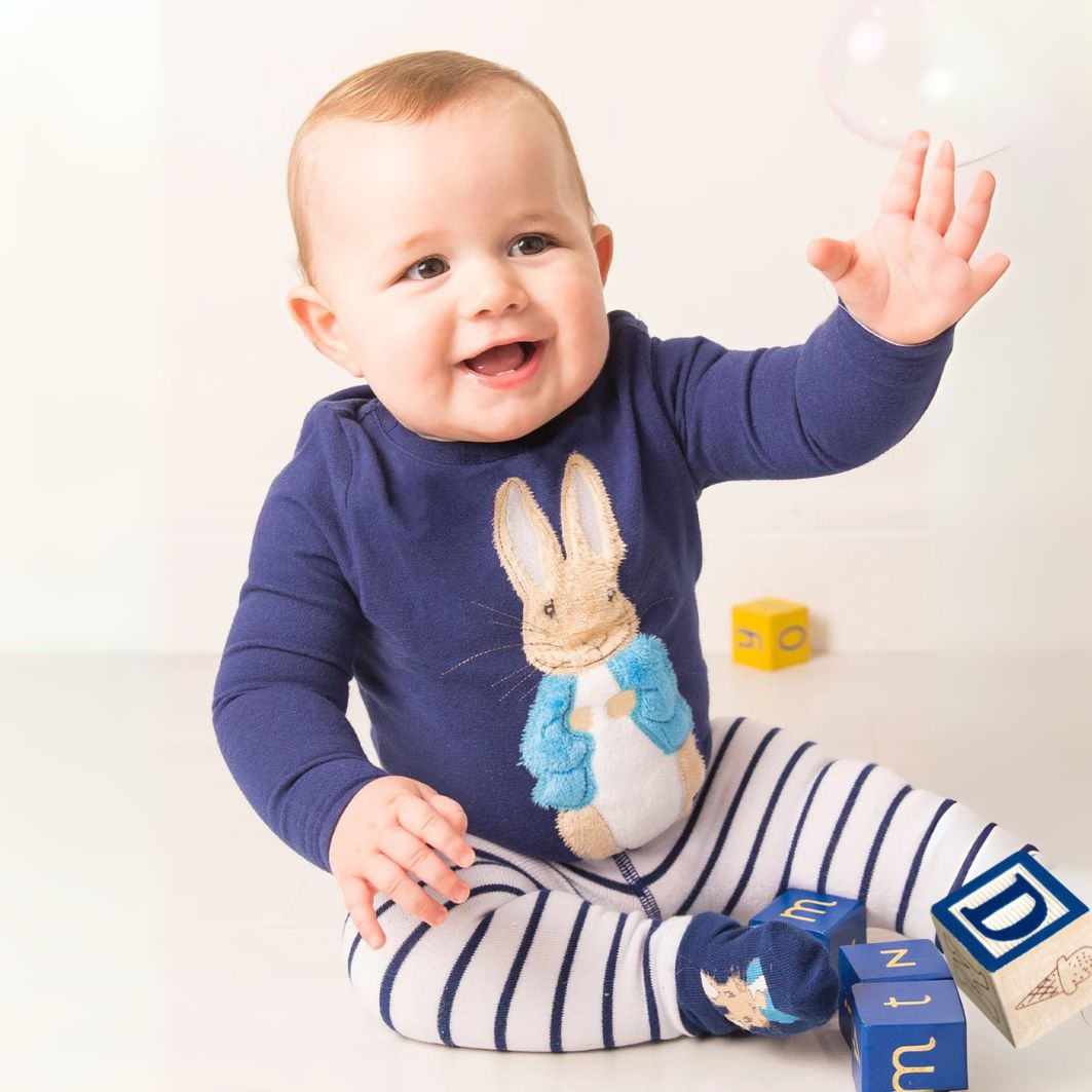 Baby wearing a blue outfit with a rabbit design, sitting on a white surface with wooden blocks.