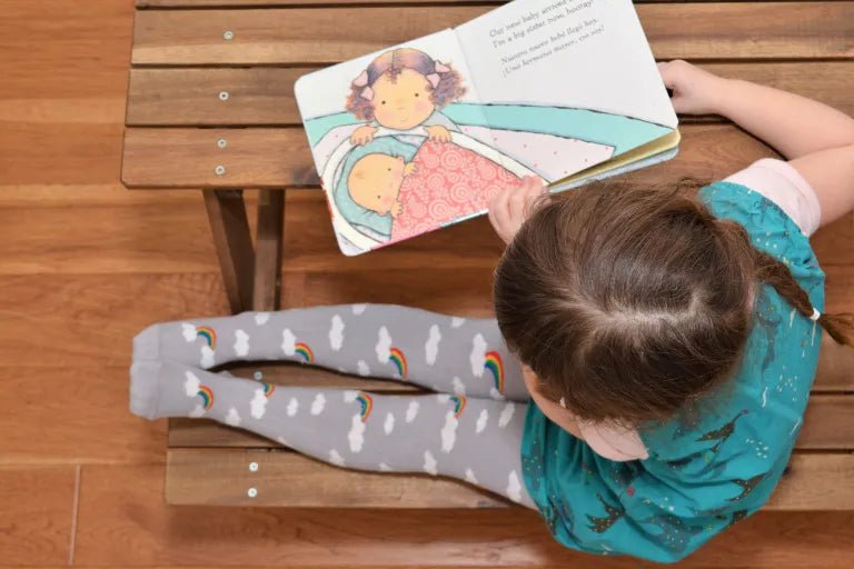 Child reading a book with colorful illustrations on a wooden floor.