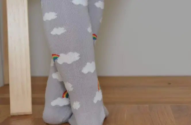 Gray leggings with cloud and rainbow pattern worn by a person on a wooden floor.