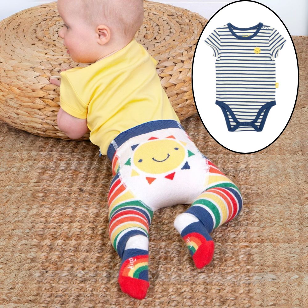 Baby wearing a yellow shirt, rainbow striped leggings, and colorful socks on a woven mat.