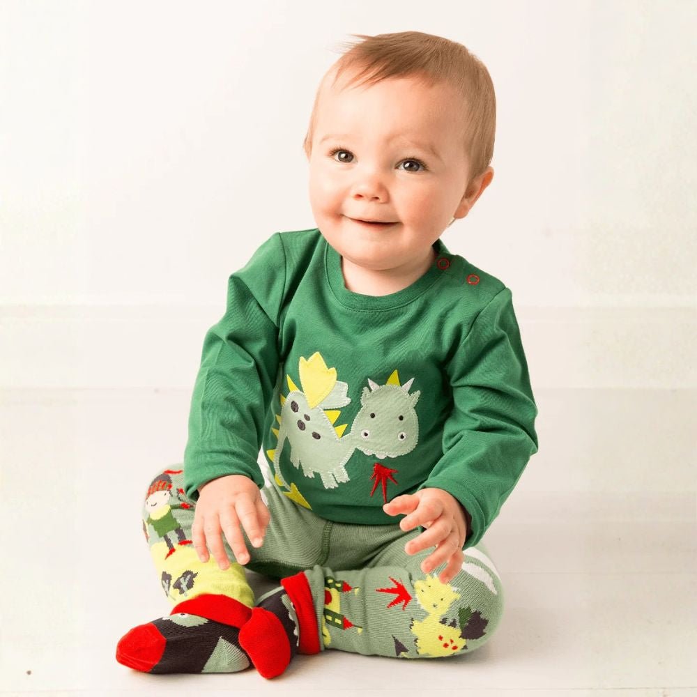 Baby wearing a green shirt with dinosaur designs on a white background