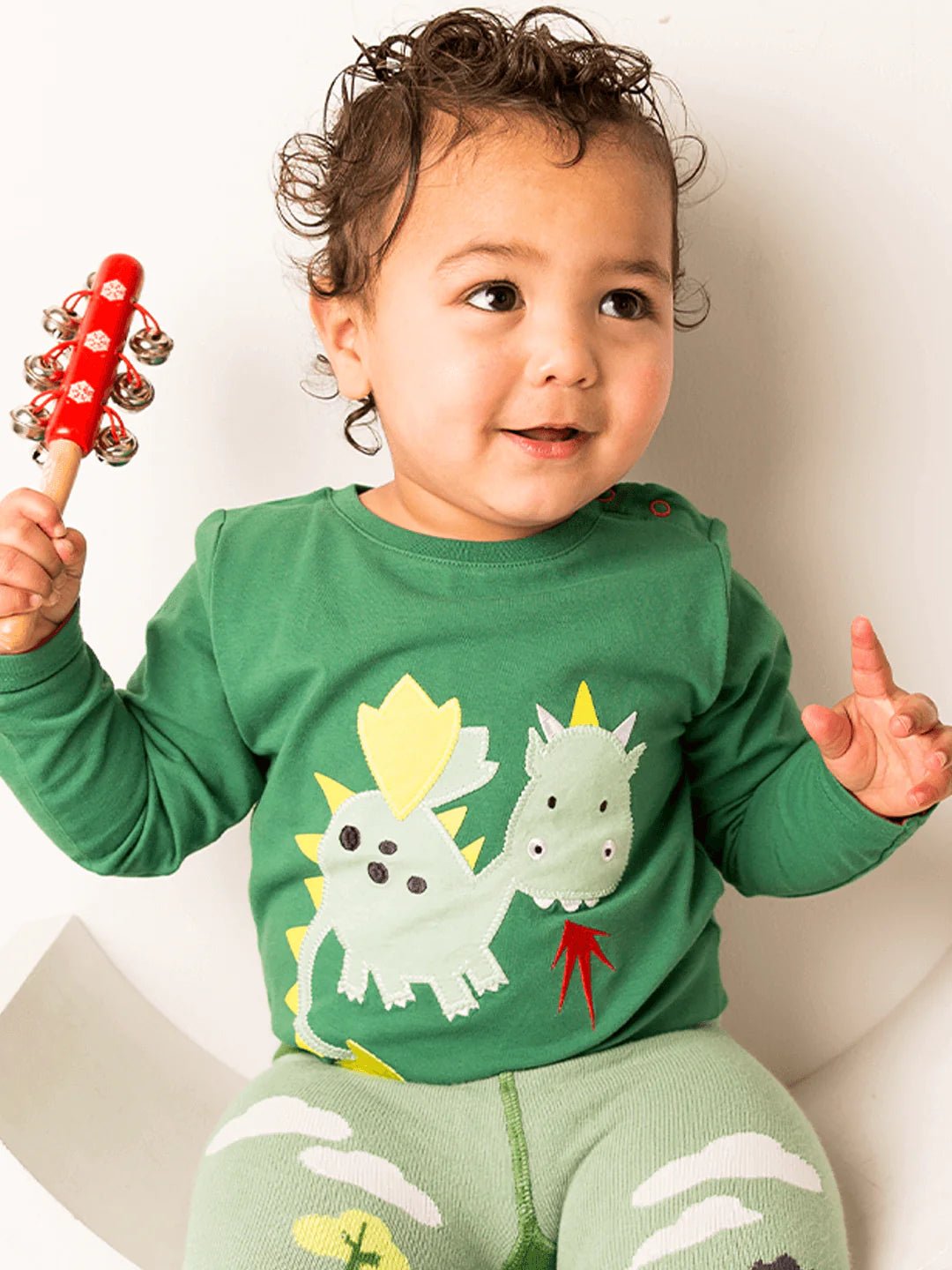 Child wearing a green outfit with dinosaur designs, holding a red toy.