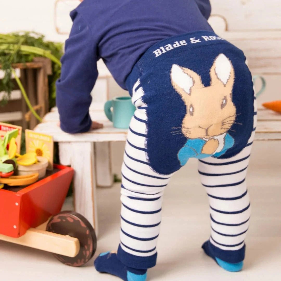 Child wearing a navy blue outfit with a rabbit design, standing on a white surface with toys around.