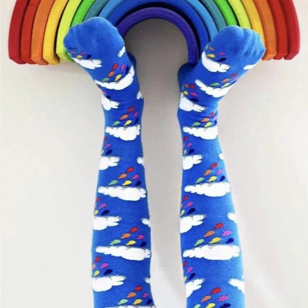 Blue socks with cloud and rainbow pattern held up against a rainbow-colored arch.