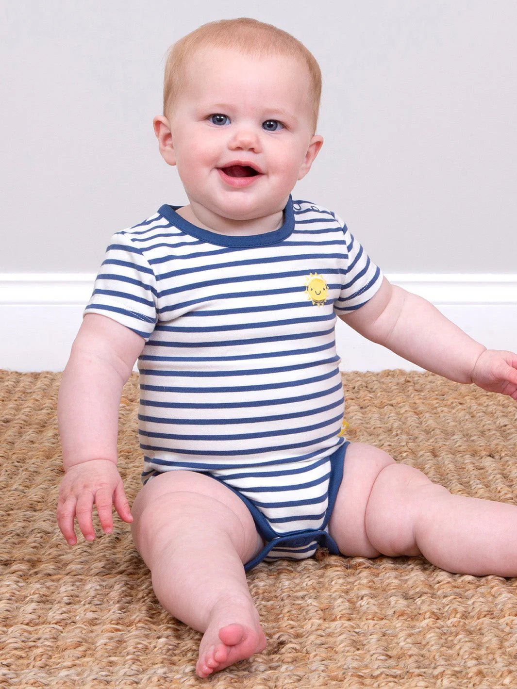 Baby wearing a blue and white striped onesie sitting on a carpeted floor.