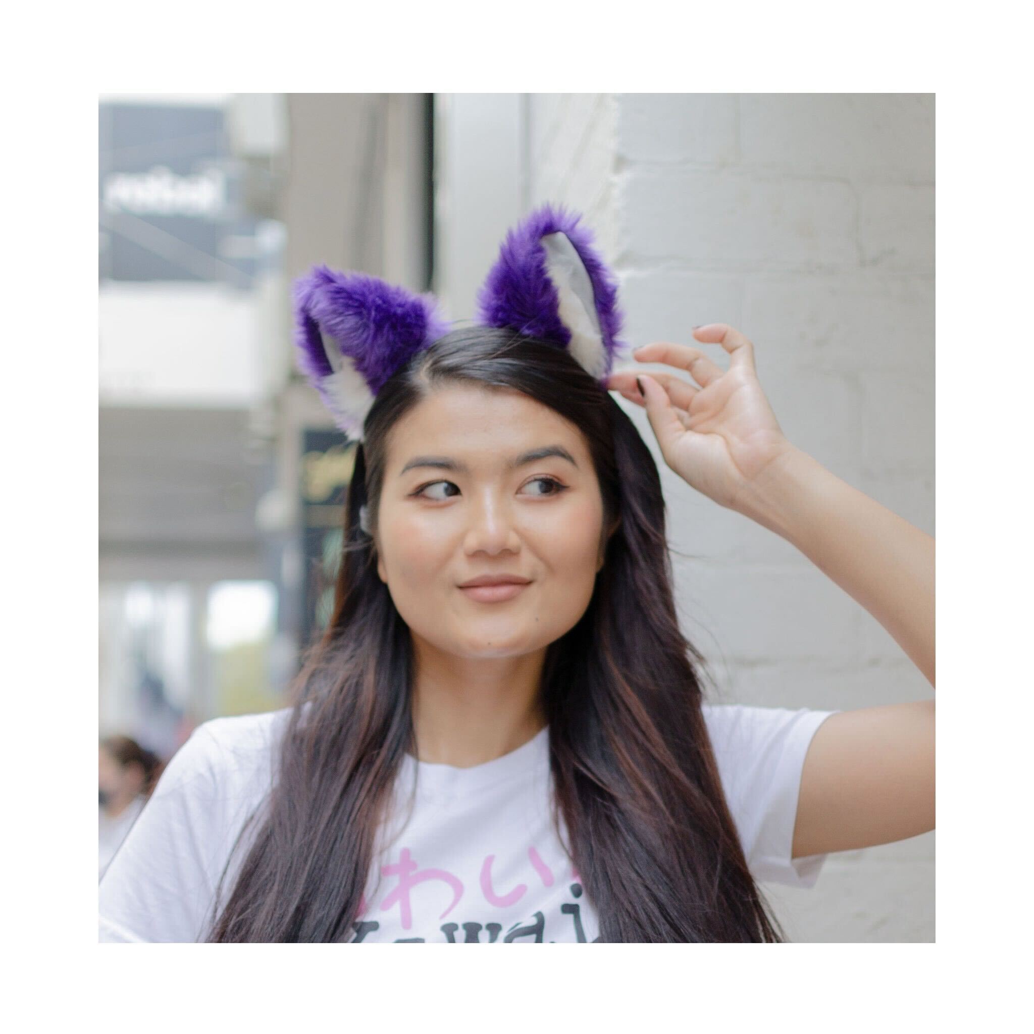 Young woman with long dark hair wearing purple and white furry cat ears and a white kawaii graphic t-shirt