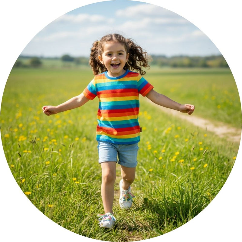 Girl in a field wearing a bright colourful rainbow t-shirt form Frugi
