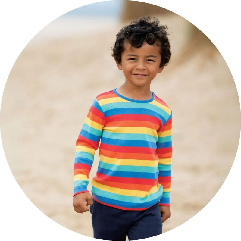 Boy in long sleeve rainbow top from Frugi on the beach