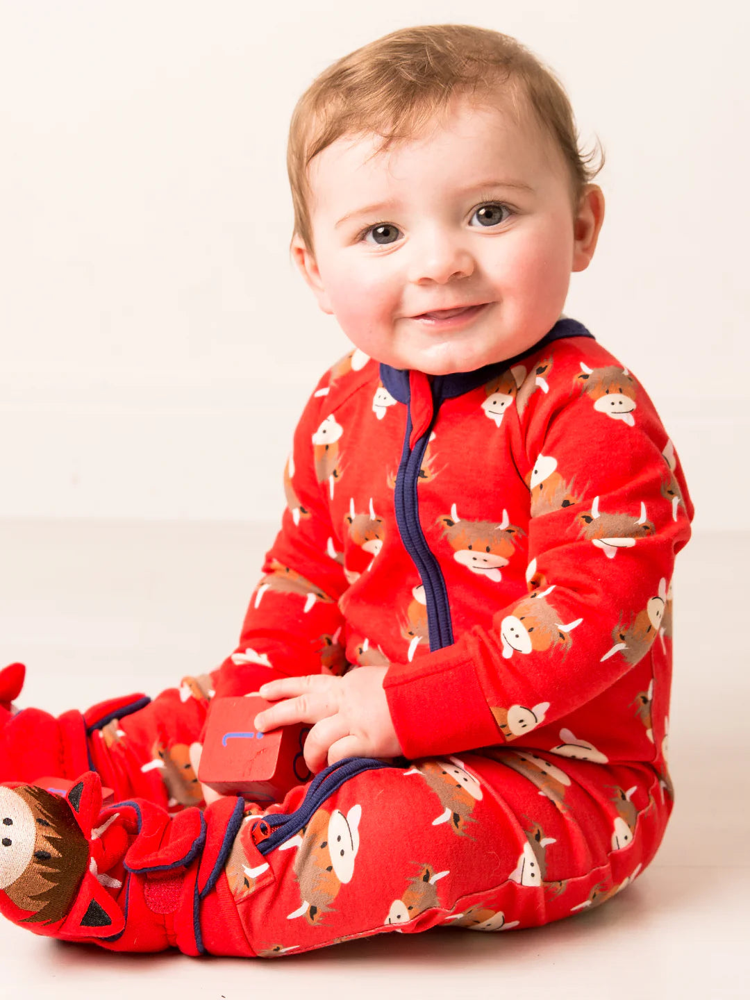 Baby wearing a red pajama with animal patterns on a white background