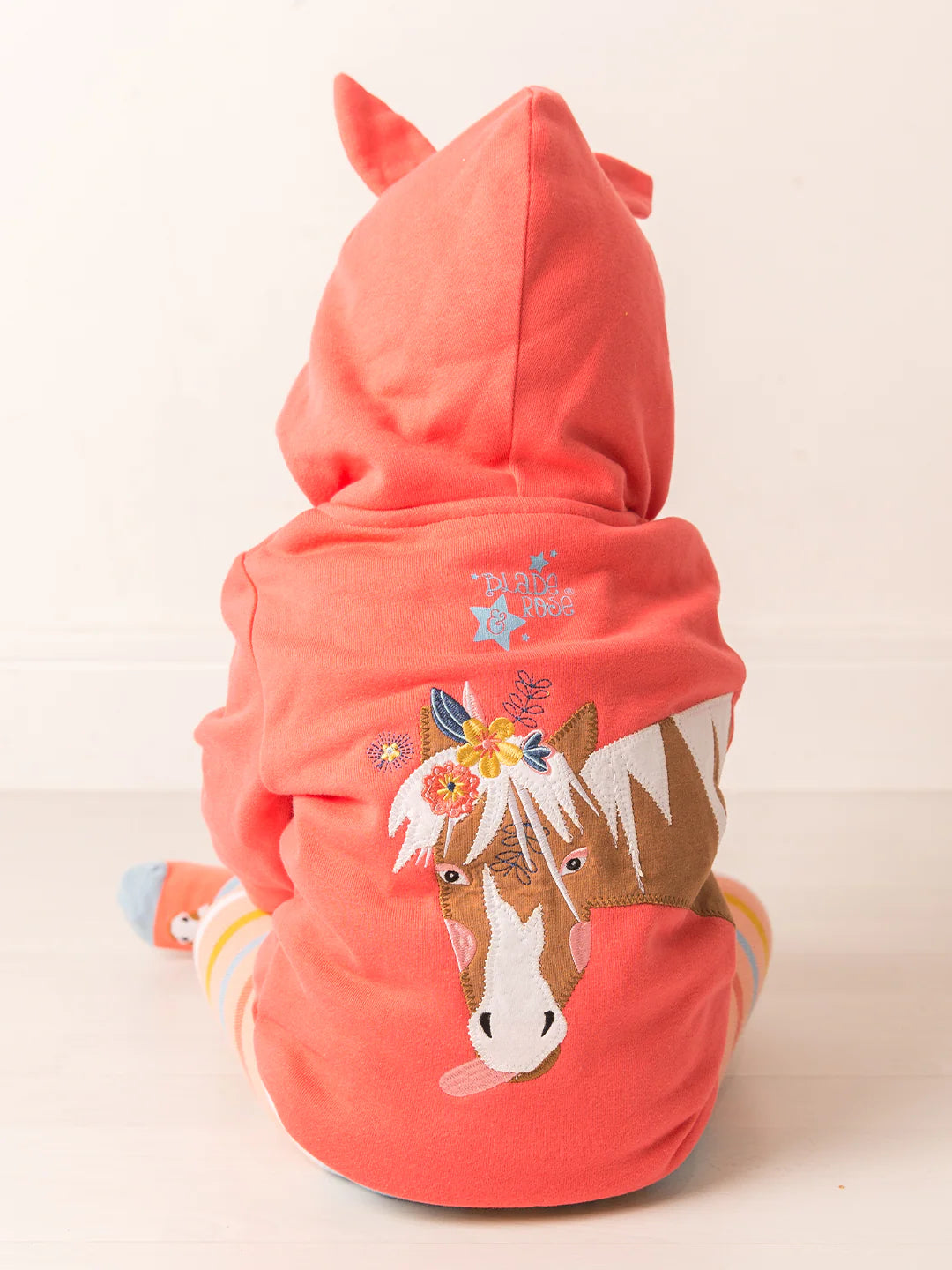 Coral-colored hoodie with horse design on a light beige background