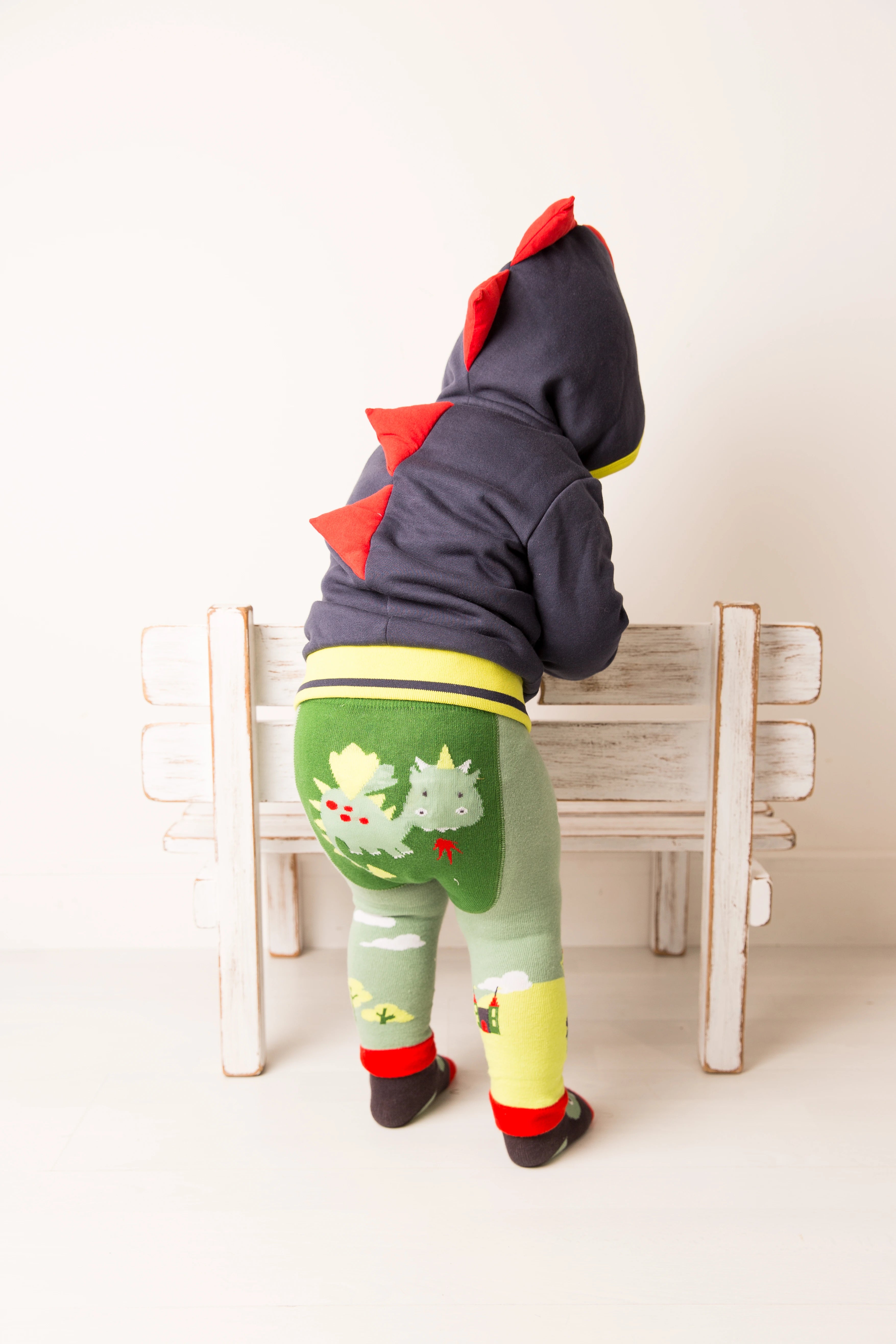 Child wearing a dinosaur-themed outfit with a hoodie and leggings, standing on a white background.