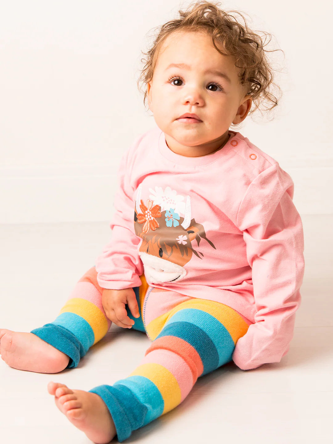 Child wearing a pink hoodie with a cartoon design and colorful striped leggings on a white background