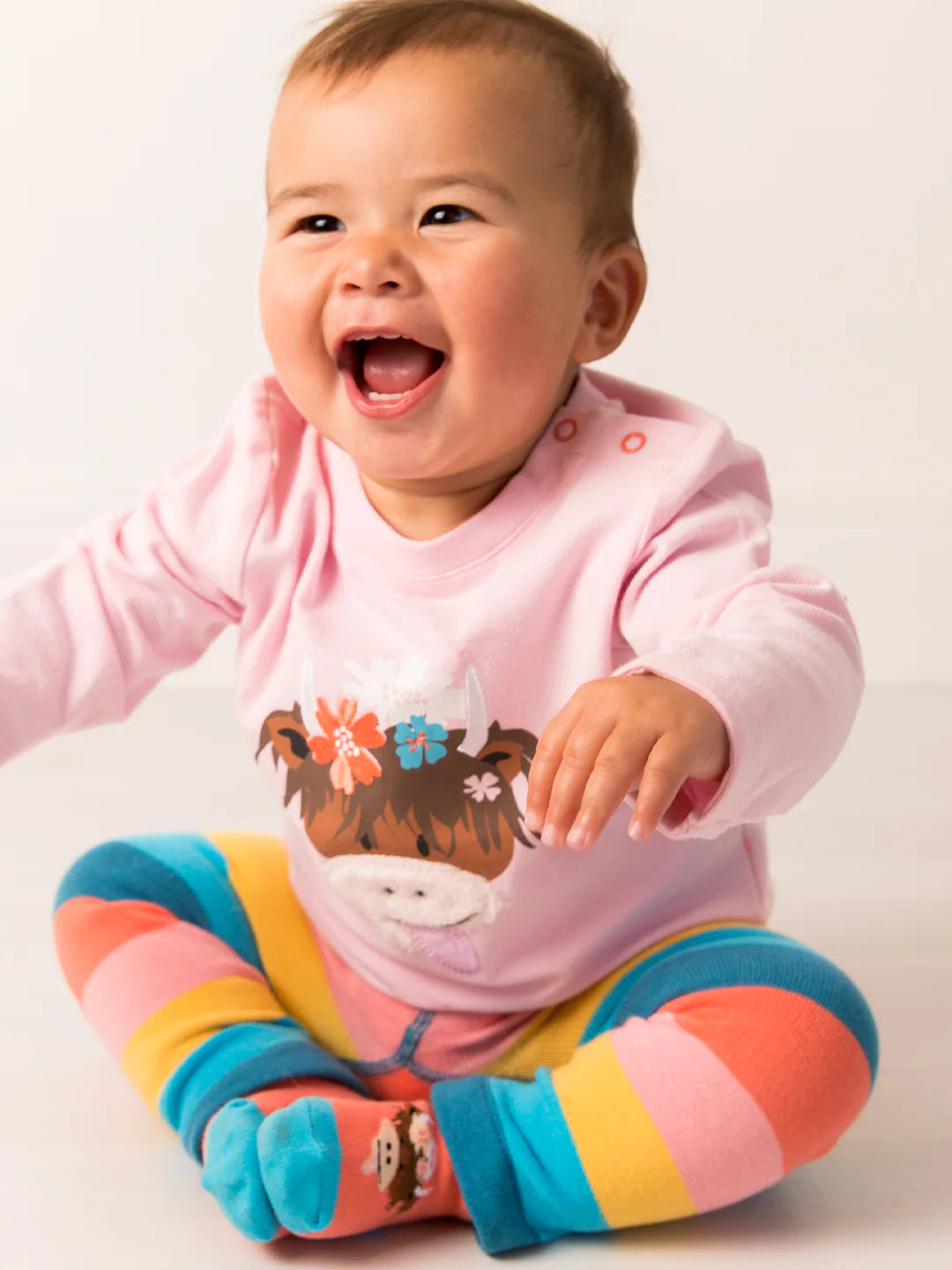 Baby wearing a pink outfit with a cartoon design and colorful socks on a white background