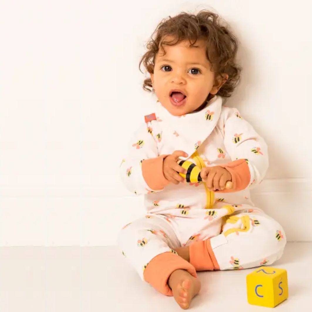 Baby wearing a white onesie with colorful patterns, sitting on a white surface.