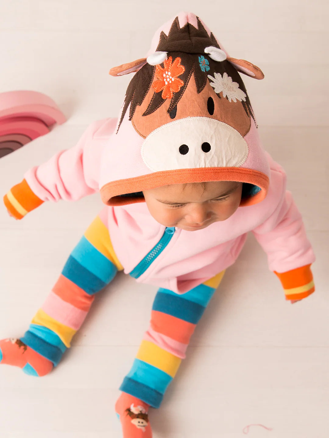 Baby in a colorful animal-themed outfit with a pink hoodie and striped pants on a white background