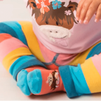 Baby wearing a pink outfit with a cartoon design and colorful socks on a white background