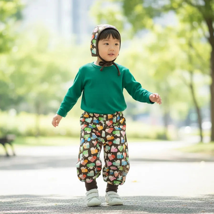 Child in a green sweater and colorful pants standing in a park.