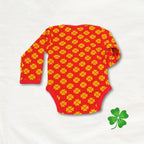 Red baby onesie with yellow pattern on a light gray background, featuring a green shamrock icon.
