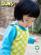 Child wearing a green and white patterned outfit with blue sleeves, standing outdoors.