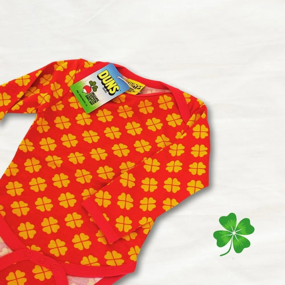 Red baby onesie with yellow clover pattern and Duns brand tag on a white background